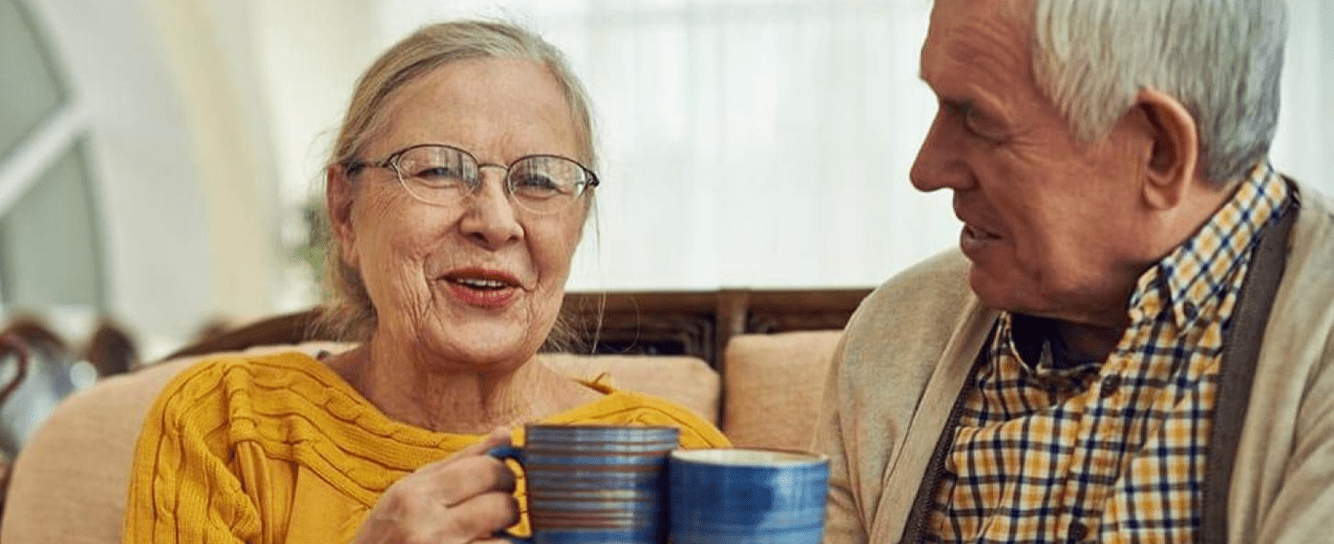 Elderly couple sitting together drinking hot drink