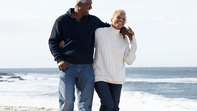 Elderly couple strolling along beach laughing together