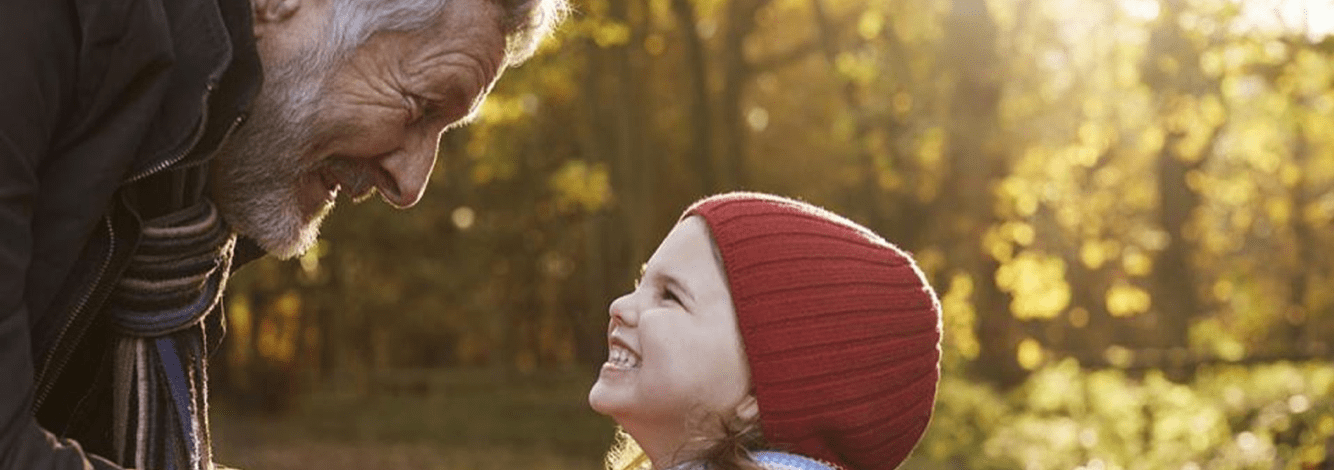Grandfather and toddler in park smiling at each other