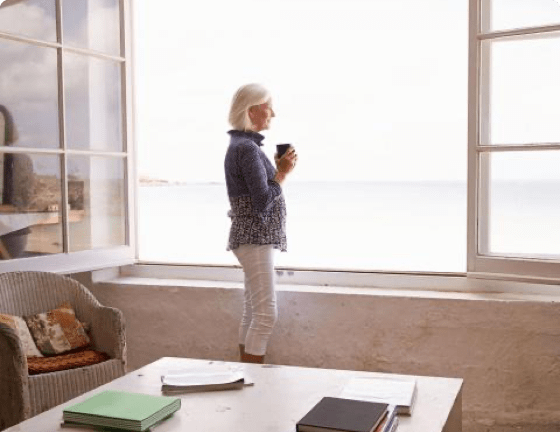 Woman standing in front of large, open window looking at the sea